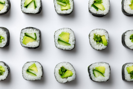 Delicately arranged sushi rolls showcase the vibrant green of cucumber and avocado, presenting a striking contrast against the pure white surface. This flat lay invites culinary appreciation.の素材