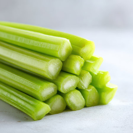 Celery sticks are arranged in a tidy pile on a white tabletop. The soft background enhances the bright green hues, inviting you to explore their crunchiness for salads or snacks.の素材