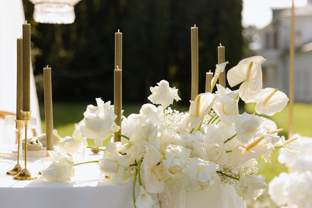 Elegant wedding centerpiece adorned with white roses and candles in a lush garden settingの写真素材