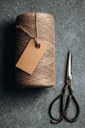 Close-up flatlay showcases a twine roll, a kraft tag, and small snips arranged artistically on a matte surface, perfect for crafting enthusiasts.の素材