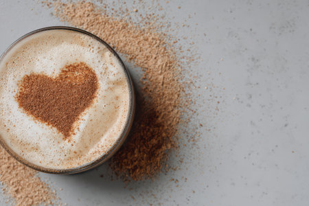 A creamy coffee drink displays heart-shaped cinnamon art on top, surrounded by scattered cinnamon powder, creating a warm and inviting scene.の素材