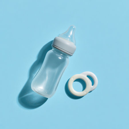 A clear baby bottle rests on a bright blue background, accompanied by a playful ring toy, capturing a cheerful moment in parenting.の素材