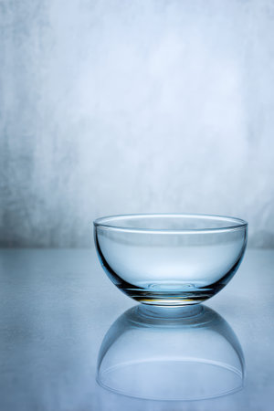 A delicate glass bowl sits gracefully on a smooth surface, reflecting soft light in a calming atmosphere. The background is a gentle mist.の素材