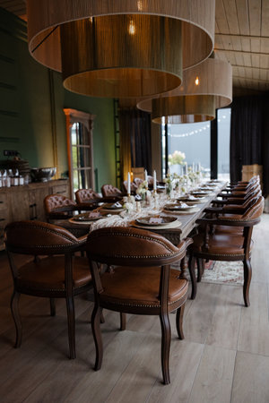 Long wooden table adorned with candles and flowers, surrounded by stylish leather chairs in a...