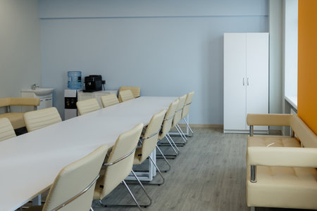 A spacious conference room with a long white table, cushioned chairs, and bright orange accents...