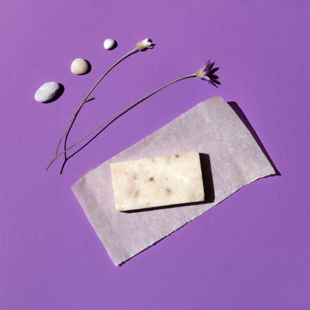 A bar of natural organic handmade cream-colored soap on a beautiful violet background surrounded by sea stones and flowers close-up, top view. Abstraction, minimalism.の写真素材