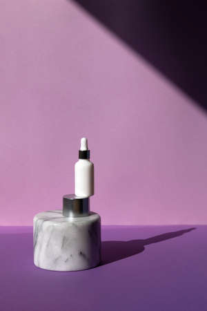 White glass bottle with cosmetic serum oil on marble and aluminum pedestal on purple background front view, closeup. Place for text.の写真素材