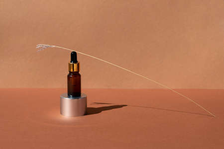 Brown glass pipette bottle with cosmetic serum on aluminum pedestal on terracotta background front view, closeup. Place for text.の写真素材