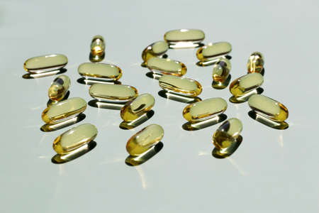 Yellow oil capsules in the rays of the bright sun close-up in bulk on a pale mint background, close-up, front view. Vitamin D, health care, polyunsaturated fatty acids.の写真素材