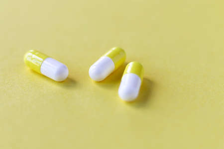 Three yellow-white capsules on a beautiful optimistic light yellow paper background. Close-up, front...