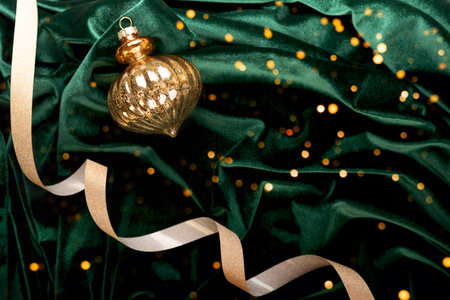 Beautiful draped dark green velvet background with gold ribbon and Christmas tree decoration, holiday lights, top view. A perfect New Year and Christmas invitation card in rich emerald color.の写真素材