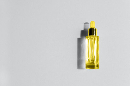 A beautiful transparent yellow bottle dropper with cosmetic serum illuminating, ultimate, gray color background. Color year 2021 the trend of the spring and summer season the fashion design industry.の写真素材