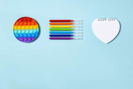 Popular silicone push up toy anti-stress circle   rainbow colors, felt-tip pens and notebook in the form heart, on a light blue paper background space for text, top view. Back to school concept.の写真素材