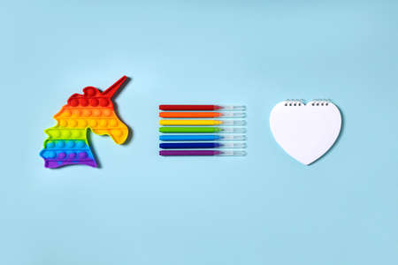 Popular silicone push up toy anti-stress unicorn   rainbow colors, felt-tip pens and notebook in the form heart, on a light blue paper background space for text, top view. Back to school concept.の写真素材