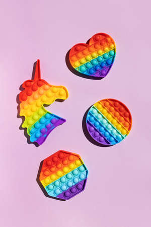 Anti stress trend toy pop rainbow colored bubble in the shape unicorn, circle, heart, octagon on a purple background vertical arrangement on a sunny day with hard shadow, copy space top view.の写真素材