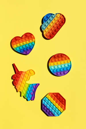 Anti stress trend push pop fidget toy pop rainbow in the shape unicorn, circle, heart, octagon, cloud on a yellow background vertical arrangement on a sunny day with hard shadow, top view.の写真素材