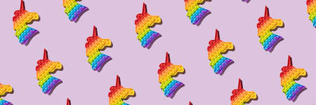 Seamless pattern banner anti stress popular push pop fidget toy pop up rainbow colored  wrap in the shape unicorn on a purple background on a sunny day with hard shadow, top view diagonal.の写真素材