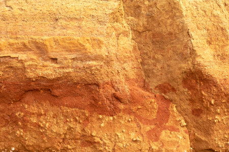A vertical sand wall texture of yellow-orange ocher sandstone on the coast, on a sunny day, natural...