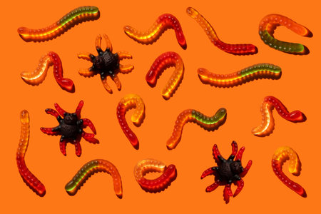 Halloween jelly beans in the shape of worms and spider on an orange background with a hard shadow. Festive sweets pattern, candy gummy trick or treat worm shaped.の写真素材