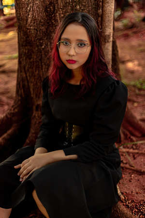 Young caucasian dark haired girl with red streaks in black dress outfit with corset belt and glasses...