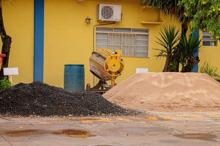 Yellow concrete mixer equipment for production of concrete under construction with sand and gravel