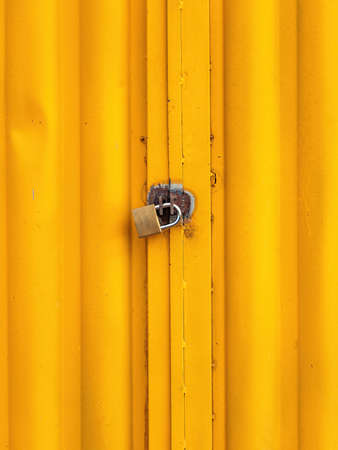 golden padlock locking a yellow metallic gateの写真素材