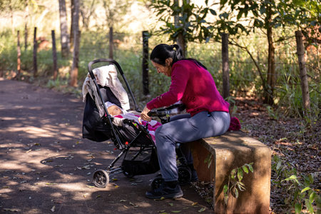 closeup of mother sitting on park bench interacting with her baby in strollerの写真素材