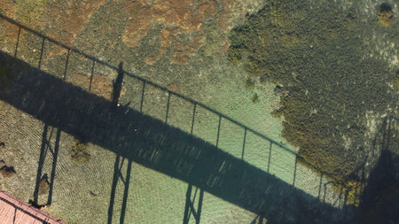 Conceptual aerial photograph showing the shadow of a wooden walkway and a passerby projected onto...