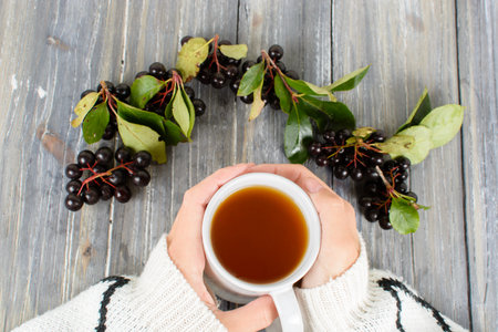 Chokeberry mug in hand on a wooden background in autumn still lifeの写真素材