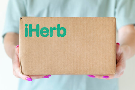 Abu Dhabi, UAE - October 15, 2021: iHerb cardboard box in woman hands. Delivery of goods in a box