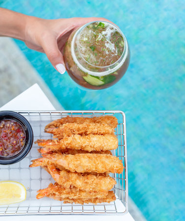 Breaded shrimps with chili sauce, slice of lemon and cocktail in hand served at the swimming poolの写真素材