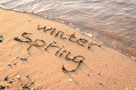 Spring is coming concept - inscription Winter and Spring on a beach sand, the wave is almost covering the word Winterの写真素材