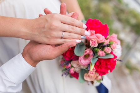Couples hands wearing their wedding rings resting on the wedding bouqetの写真素材