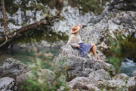 A girl sitting on the stone among the mountains and looking at the river. Woman sits near the mountain river enjoy the view. The rapids on the river.の写真素材