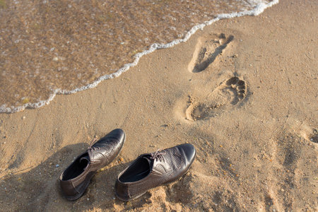 Work Life Balance Concept, Businessman take off his Working Shoes and leave it on the Sand Beach for Walk into the Sea on Sunny Day. Top View.の写真素材