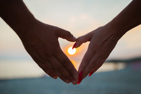 Heart shape made with hands at sunset.
