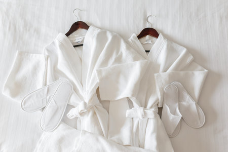two white bathrobes and slippers on the bed in room.の写真素材