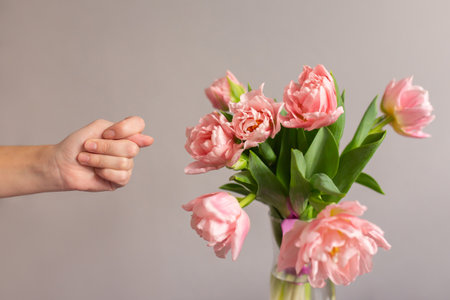 Female hand is showing a Fig gesture. Bouquet of pink tulips in a glass vase on the table. Humor conceptの写真素材