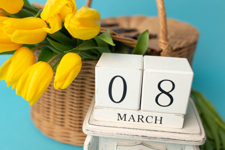 international women day. Wooden calendar 8 of march and yellow tulips in a basket of vines on blue background.の写真素材