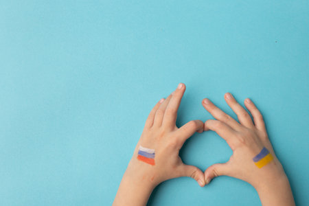 Children's hands with the flags of Russia and Ukraine are folded with their hearts as a symbol of...
