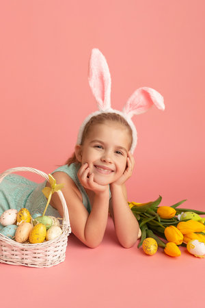 Closeup portrait of a smiling little girl on a pink background with an easter decor. Cute happy...