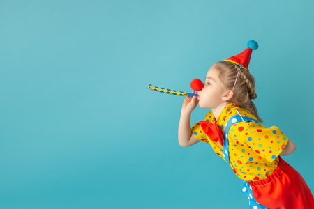Funny kid clown against blue background. Happy child playing with festive decor. Birthday and 1 April Fool's day concept.の写真素材