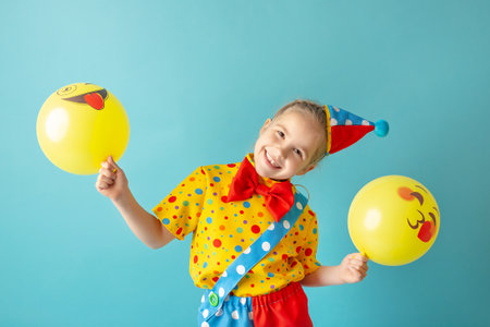 Funny kid clown against blue background. Happy child playing with festive decor. Birthday and 1 April Fool's day concept.の写真素材