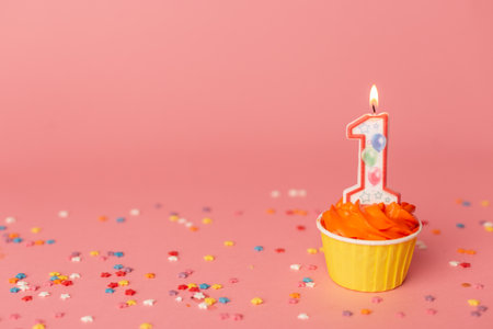 Number 1 candle in a cupcake against a pastel pink background. First bithday cake.の写真素材