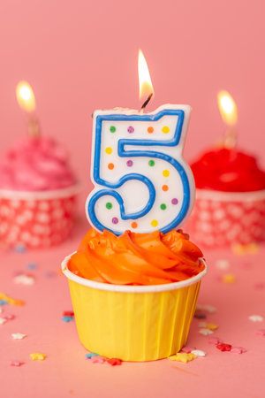 Cake for the fifth birthday. Candle number 5 in a cupcake among colorful cakes on a pink background.の写真素材
