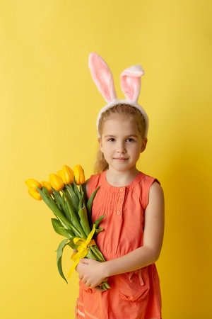 Beautiful cute little girl in Easter bunny ears smiling and holding spring bouquet of tulips on a...