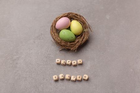 Minimal Easter concept. Nest with three colorful easter eggs with text Happy Easter on gray background.の写真素材