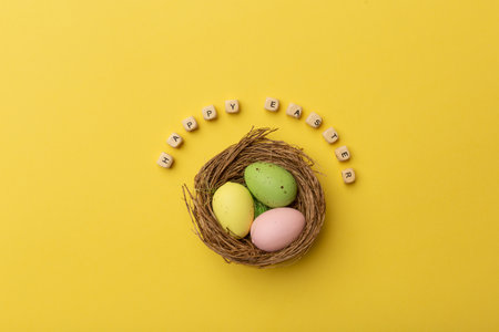 Minimal Easter concept. Nest with three colorful easter eggs with text Happy Easter on yellow background.の写真素材