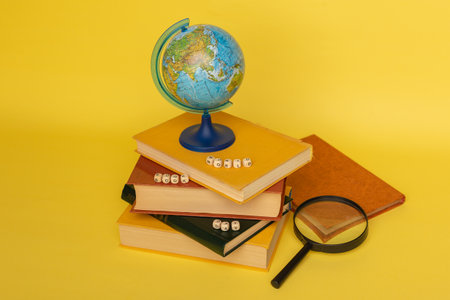 Stacks of books, globe, magnifying glass and wooden text World Book Day on the yellow background....