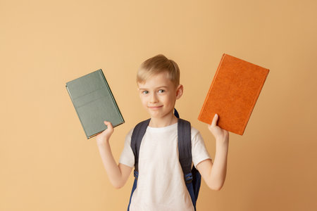 Cute smiling child with a backpack holding books in preparation for school on a beige background.の写真素材